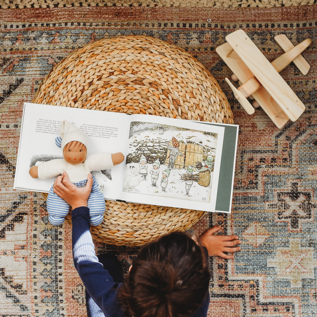 A child reading Children of the Forrest by Elsa Beskow, holding a Waldorf doll.