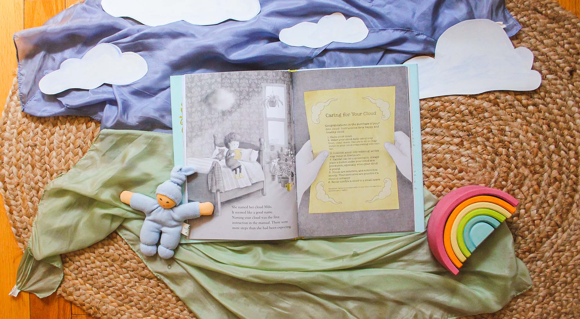 Lizzy and the Cloud book surrounded by play silks, wooden rainbows, and clouds.