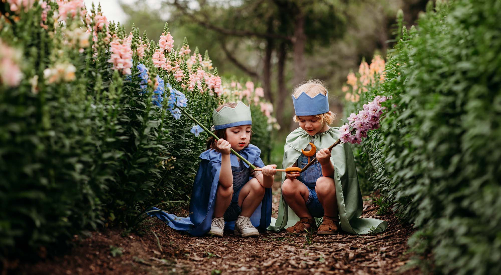 Children dressed in play silks sit in a field of flowers.