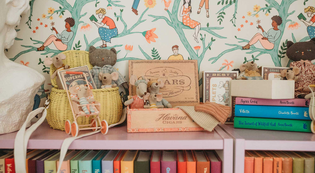 A collection of Maileg Mice sit on a colorful bookshelf.