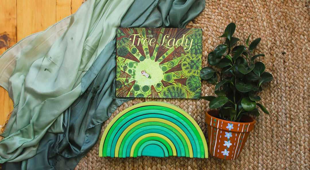 The Tree lady book sits on a playsilk with a terracotta planter and green wooden rainbow.