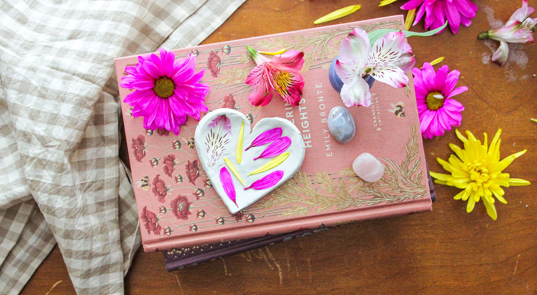 A clay trinket dish sits on a stack of books with fresh flowers.