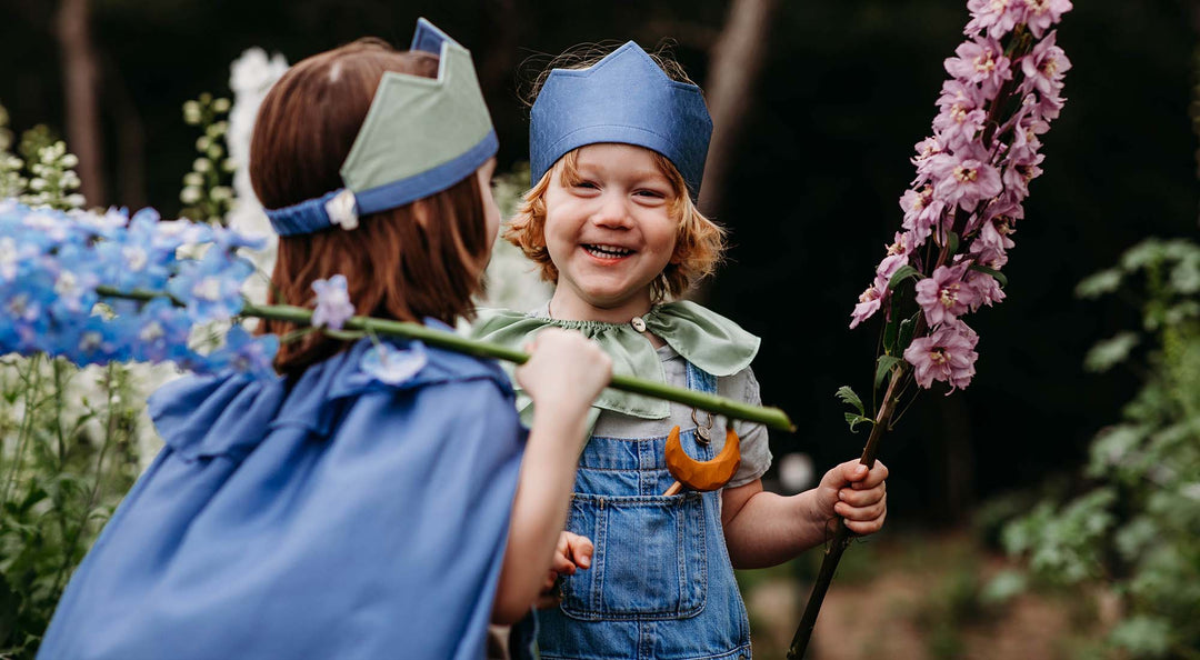 Two kids are playing dress up amongst tall flowers.