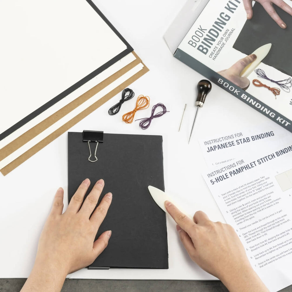 A person folding paper from the Kikkerland Book Binding Kit.