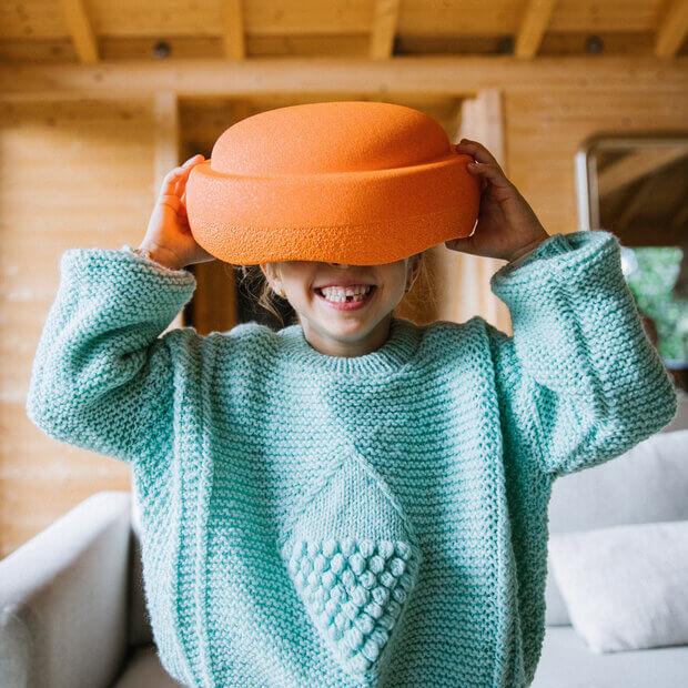 A child holds an orange Stapelstein stepping stone on their head.