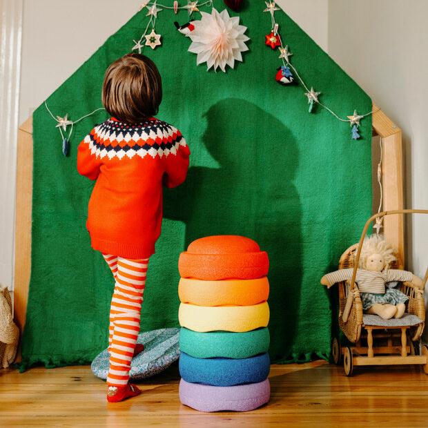 A child steps on the Stapelstein balance board to hang a holiday decoration. A stack of Stapelstein stepping stones are next to him.