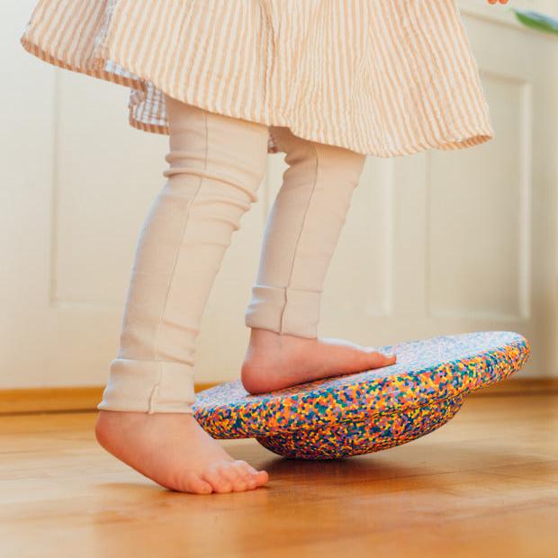 A child stepping onto a classic confetti Stapelstein® Balance Board.