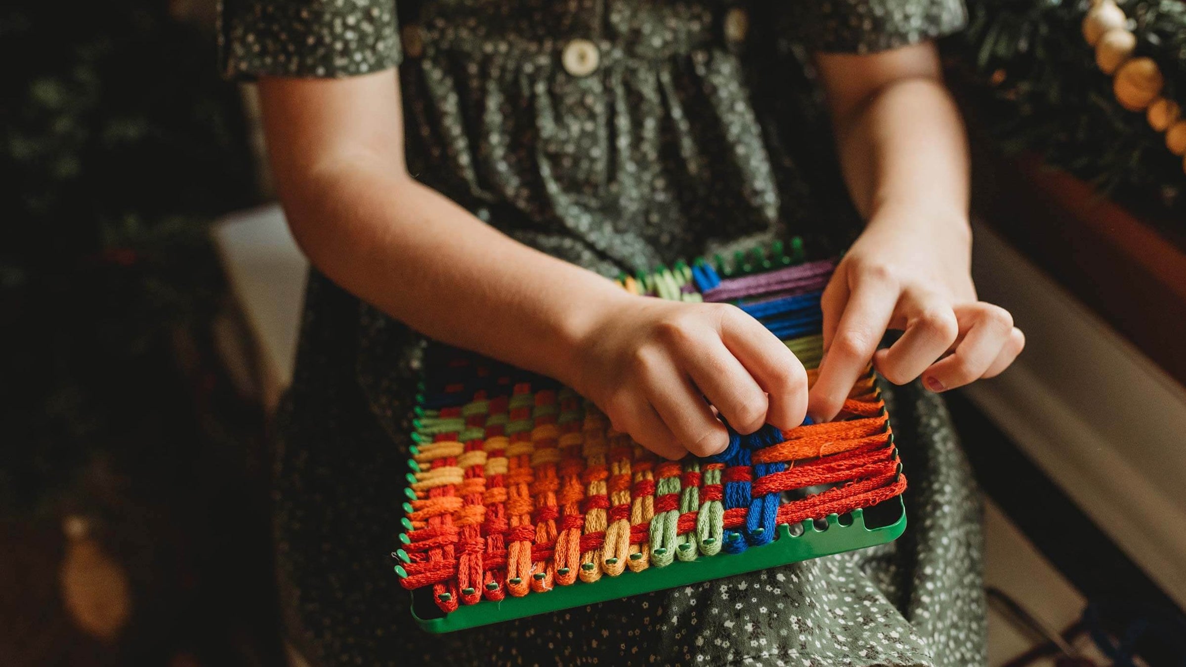 Child in a green dress hand knitting on a loom