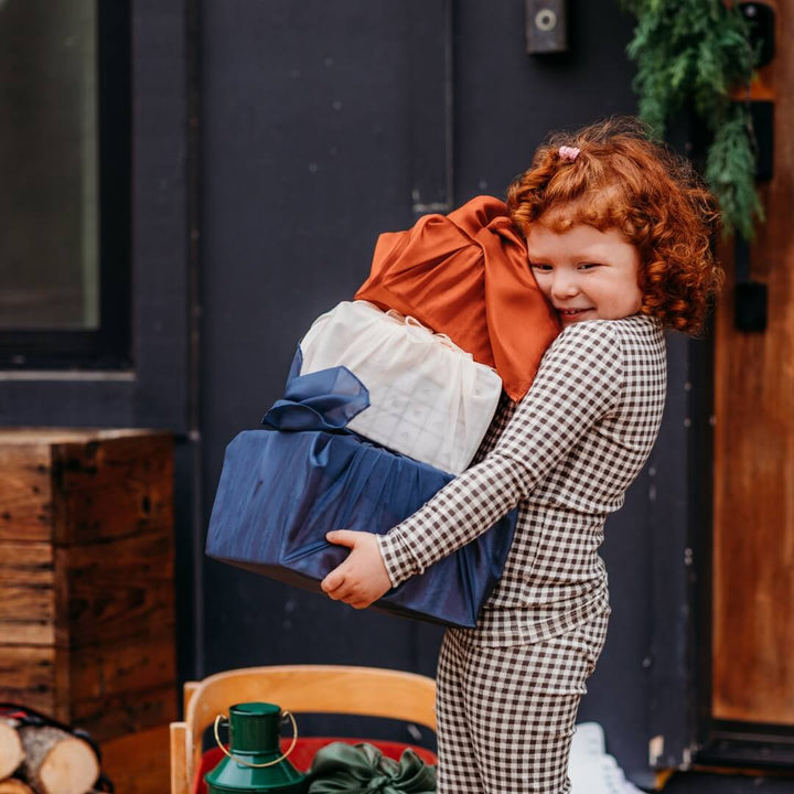 A girl holds boxes wrapped in the Bella Luna Toys 2024 Holiday Playsilk Collection.