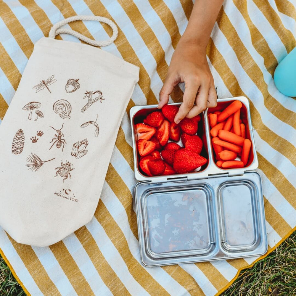 A child has strawberries and carrots as a snack with the Bella Luna Toys Nature Treasure Hunt Lunch Bag.