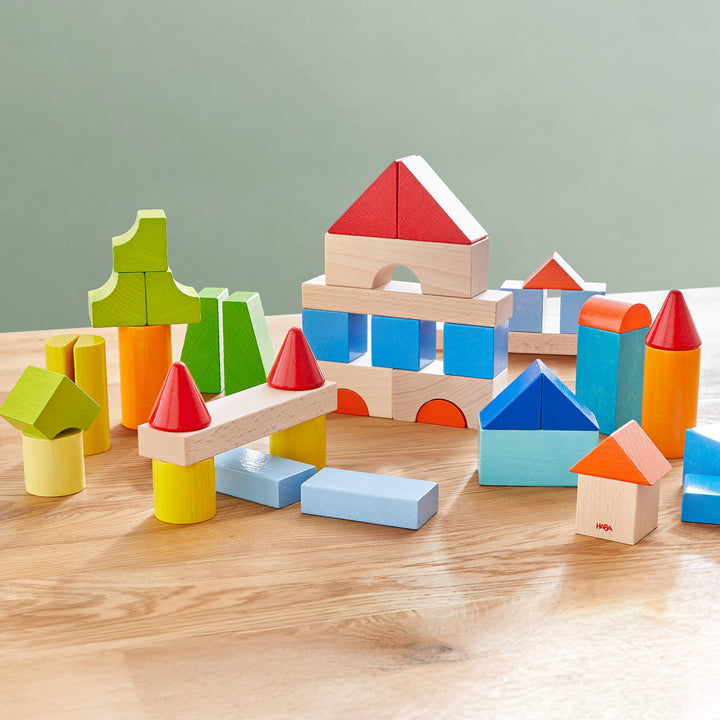 Colorful wooden building blocks in various shapes arranged on a wooden table, creating playful structures against a green backdrop.