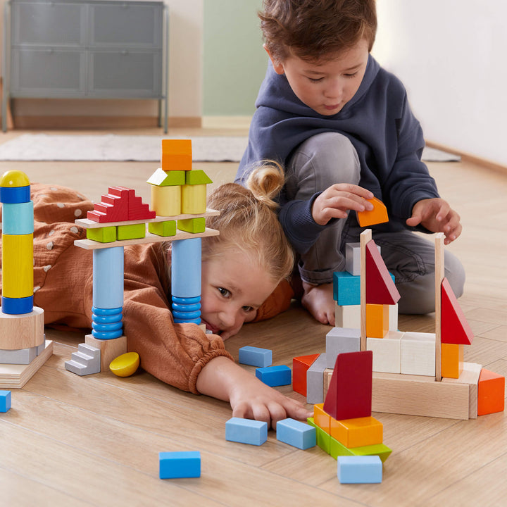 Two children play with colorful wooden blocks on a wooden floor, building structures and exploring creativity together.