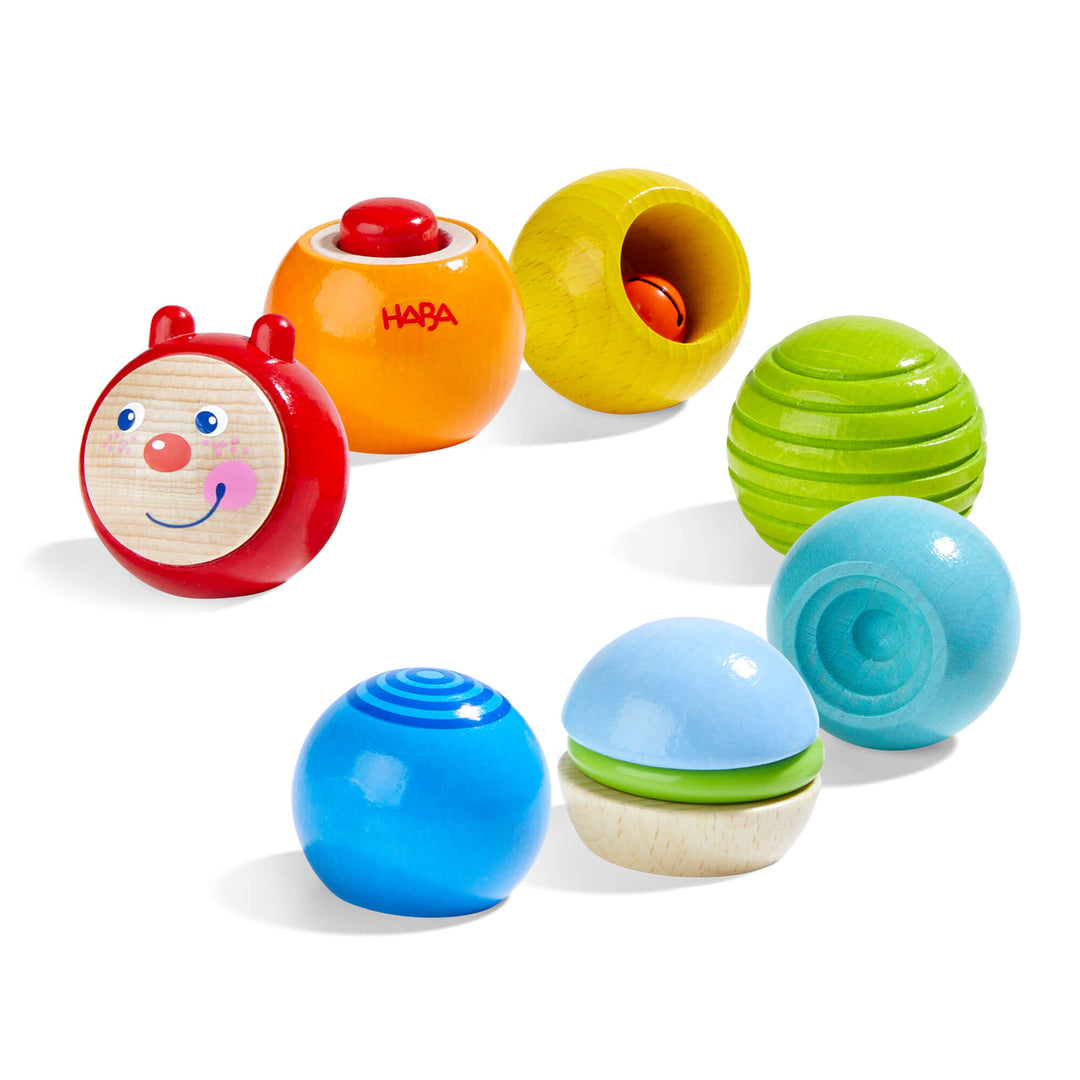 HABA Discovery Building Blocks Wooden Caterpillar with red caterpillar face, round orange wooden block with red button, yellow round wooden hollow block with red bell, green rounded wooden block with indented spirals, rounded neon blue wooden block, 3 piece natural/blue wooden block with green plastic ring, and blue rounded wooden block with bullseye printed