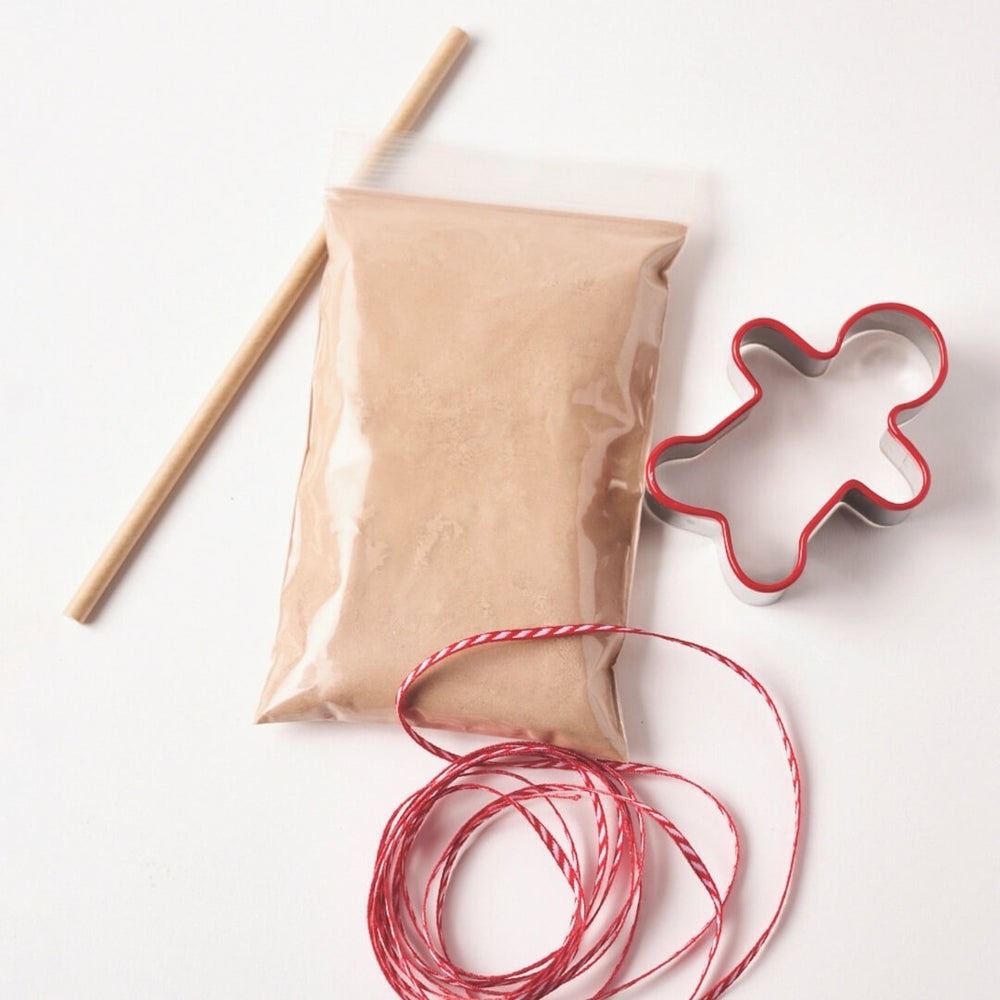 Contents of the gingerbread ornament kit including a cookie cutter, dough mix, ribbon and wooden dowel.