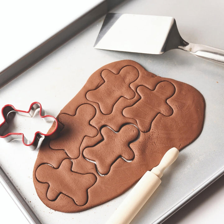 Gingerbread dough rolled out on a pan with gingerbread shapes cut out of it.