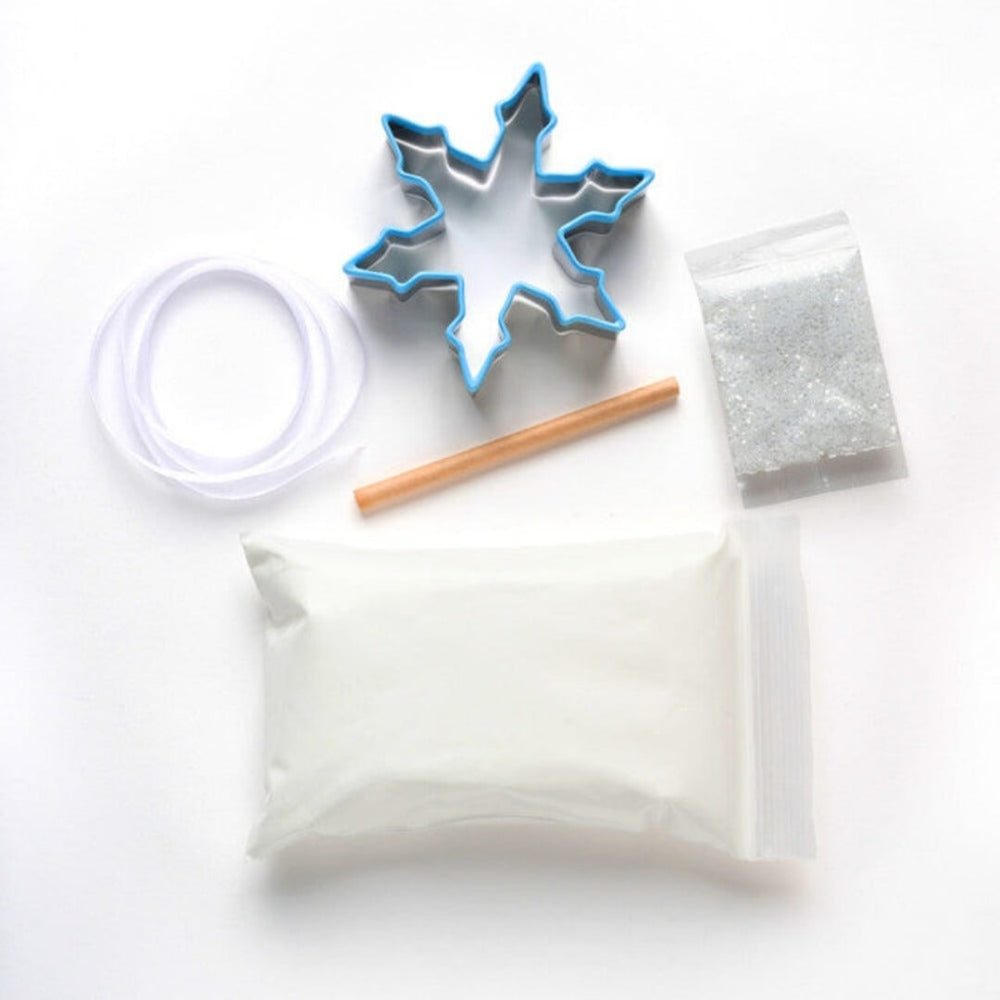 Contents of Snowflake Ornament Kit including dough mixture, cookie cutter, glitter, ribbon and a wooden dowel.