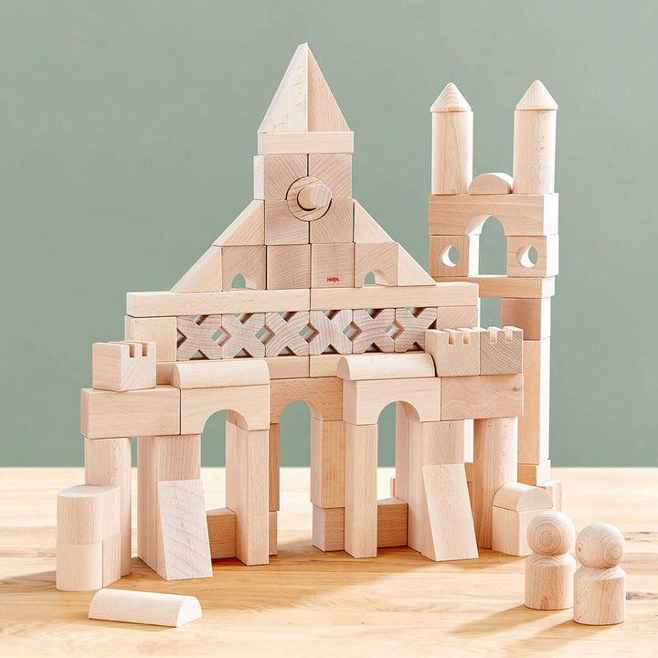 A creative arrangement of Basic Building Blocks 102 Piece Extra Large Wooden Starter Set blocks forming a castle-like structure, featuring towers, arches, and decorative panels.