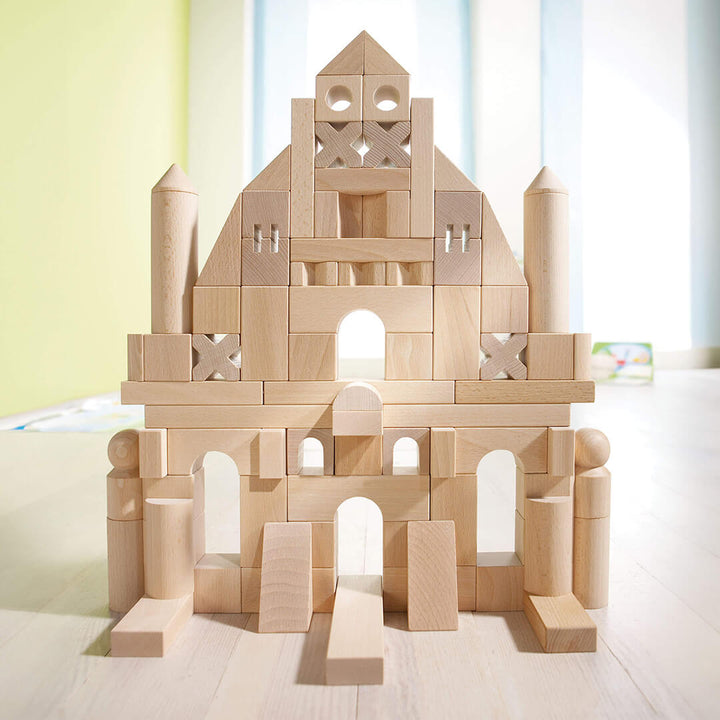 A large structure made of the Basic Building Blocks 102 Piece Extra Large Wooden Starter Set, featuring arches, towers, and a central peak, set in a bright room.