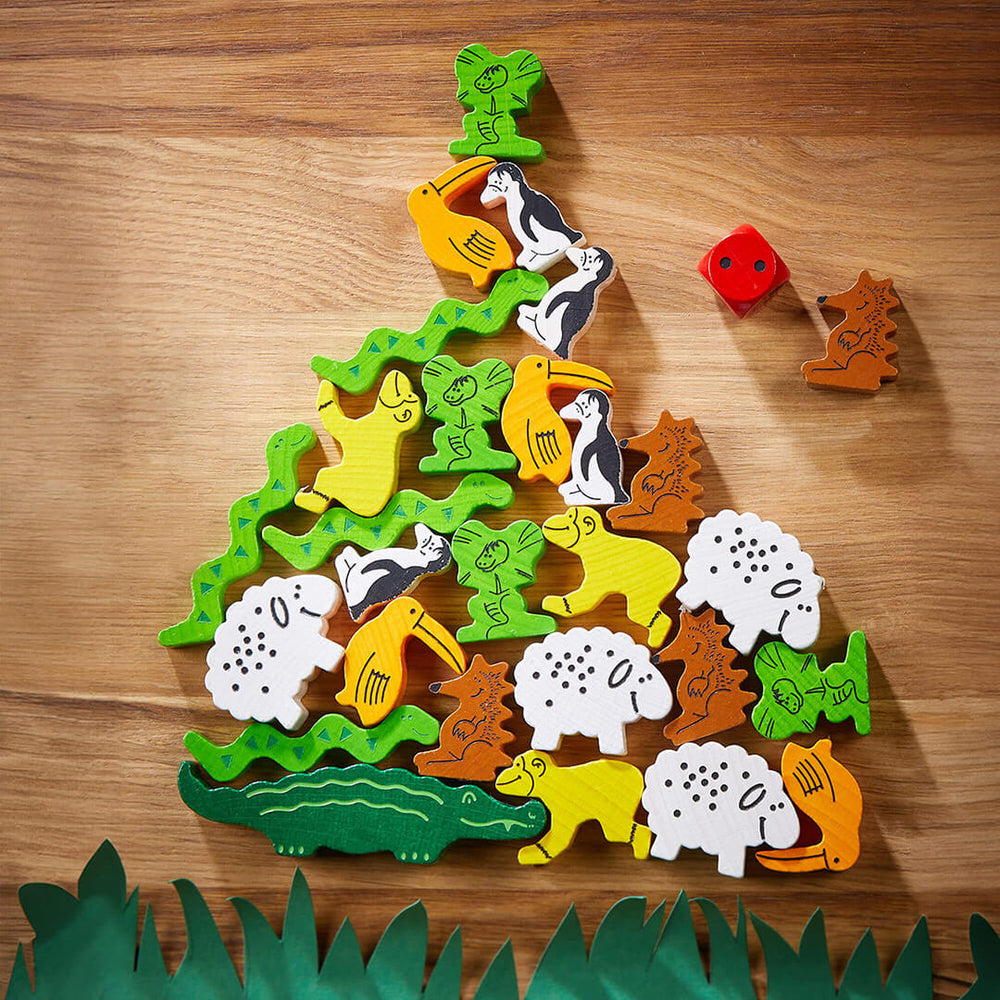 A colorful arrangement of wooden animal figures forming a pyramid shape on a wooden surface, with a red die nearby.