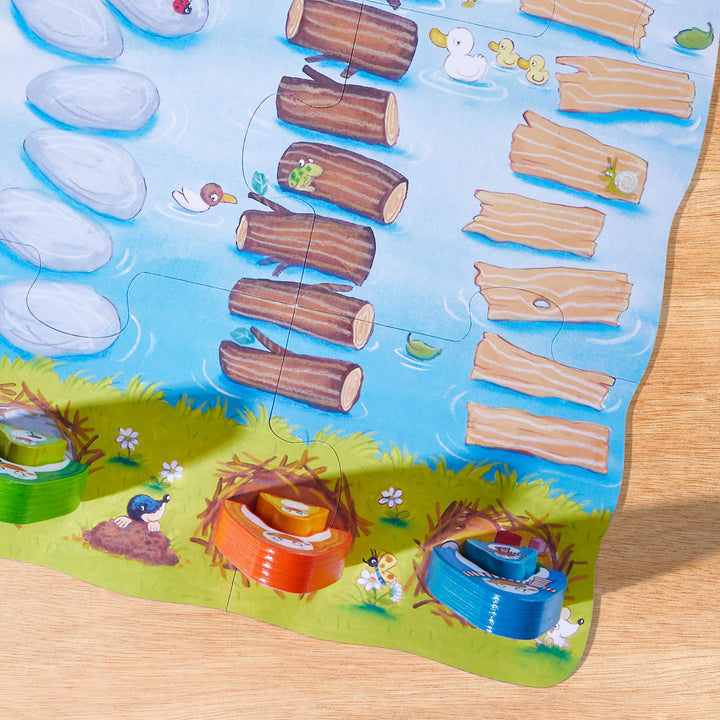 Overhead of My Very First Games Go Go Little Penguin game board with illustrated logs and rocks in a river with blue, orange, and green wooden penguin game pieces