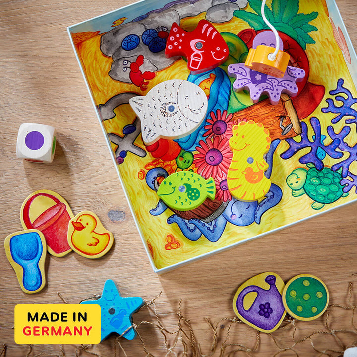 Here, Fishy, Fishy! Magnetic Game's  colorful wooden pieces featuring sea creatures and plants, with various shapes and a die on a wooden surface. Made in Germany