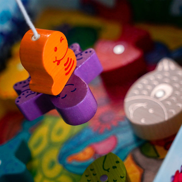 My Very First Games - Here, Fishy, Fishy! Magnetic Game's colorful wooden worm figurine hangs from a fishing line connected to a purple wooden octopus