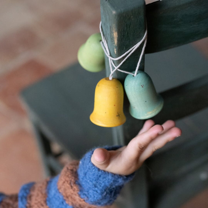 A child reaching for the Grapat Jingle Joy Bells wooden ornaments hanging on a wooden chair.