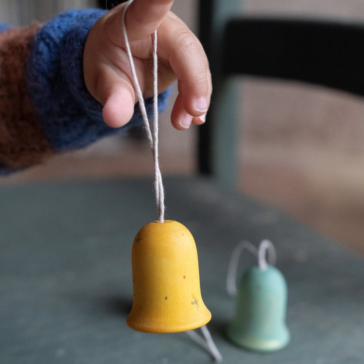 A child holding a Grapat Jingle Joy Bells wooden ornament on their finger.