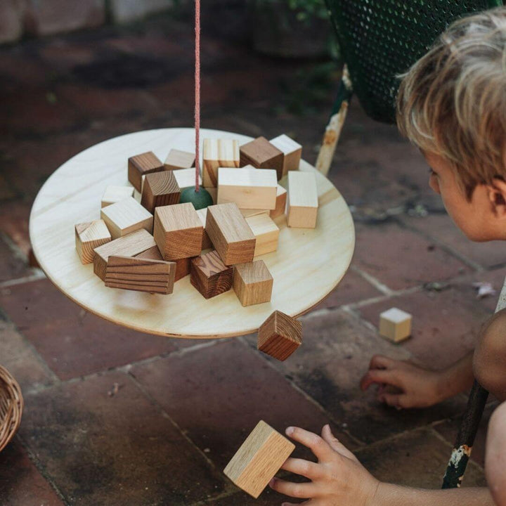 A young child filling the Grapat Wooden Pendulum Balance Board – with different shapes of wooden blocks to explore balance, motion, and physics through open-ended play and creative experimentation.