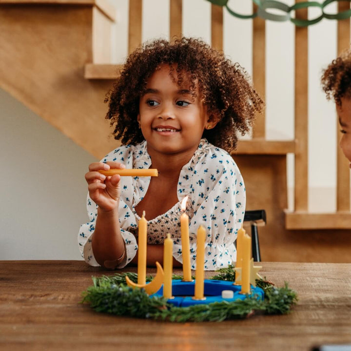 A child lights a beeswax candle in the Grimm's Over the Moon celebration ring.