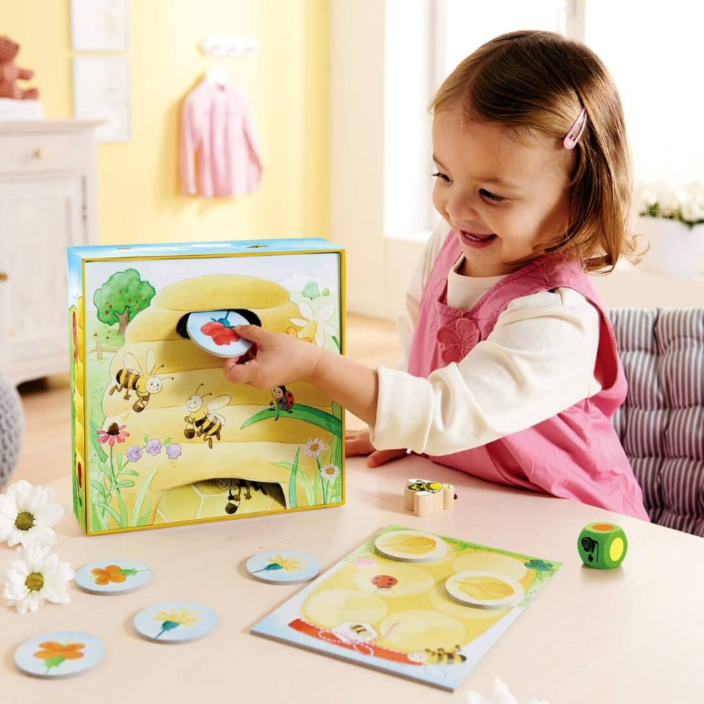 A toddler in a pink dress places a flower tile into the Hanna Honeybee game box.