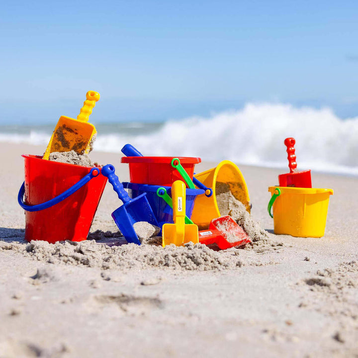 A large assorted collection of Spielstabil pails and scoops on the beach with waves crashing