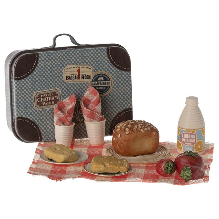 Maileg Mouse Sized Picnic Set with red and white checked blanket, a loaf of bread, 2 cups, 2 napkins, 2 stawberries, 1 tomato, 1 orange juice, 2 plates, 2 pieces of bread with wholes, and a woven charger with a blue patterned suitcase - from the side