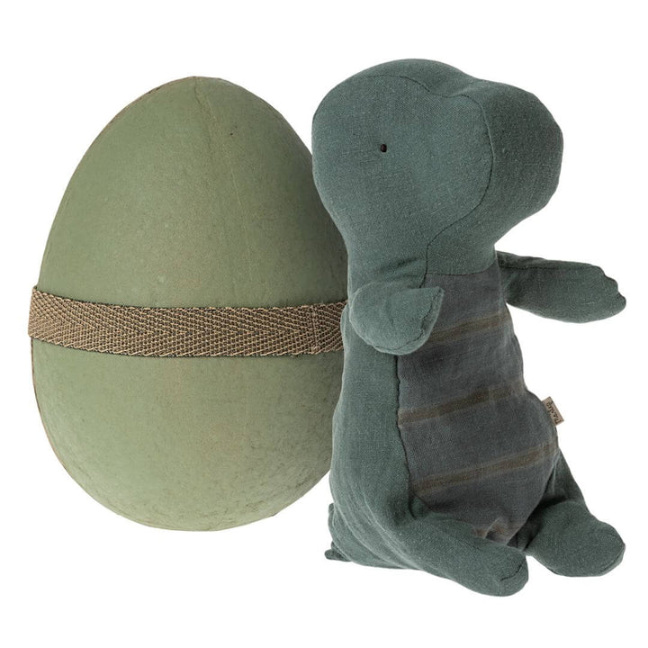 Maileg Small Gantosaurus in Egg – Dark Petrol. A soft, plush green dinosaur with a striped belly, sitting beside its matching deep green egg-shaped shell secured with an elastic band.