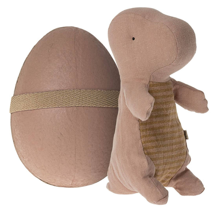 Maileg Small Gantosaurus in Egg – Old Rose. A soft, plush dinosaur toy with a striped belly, sitting beside its matching rose-toned egg-shaped shell secured with an elastic band.