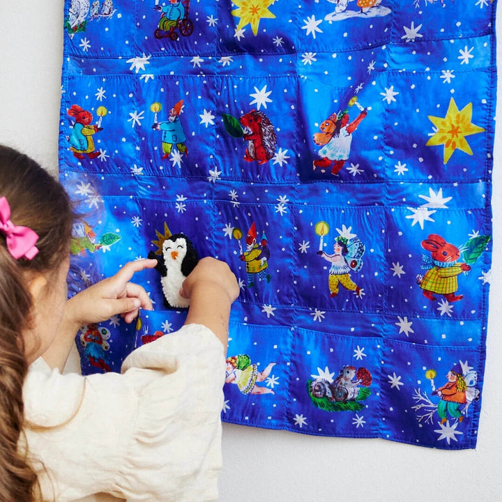 A child pulls a penguin toy out of the Phoebe Wahl illustrated pocket advent calendar by Sarah's Silks.