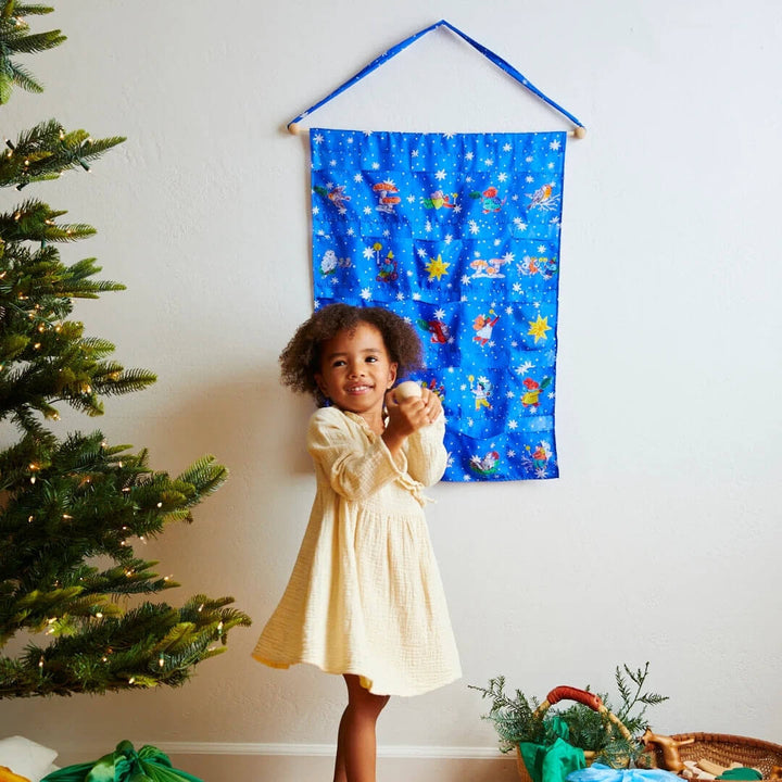 A child holding a gift stand in front of the Phoebe Wahl illustrated pocket advent calendar by Sarah's Silks.