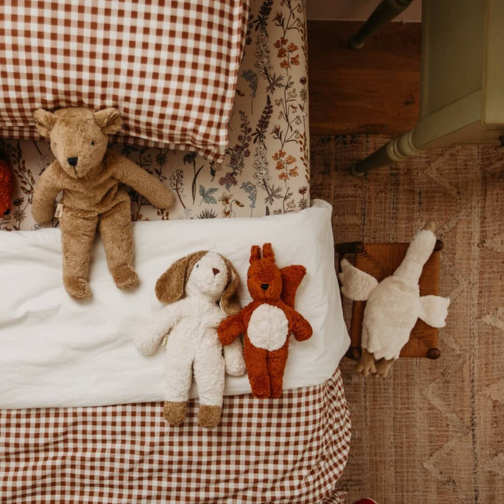 An assortment of Senger organic stuffed animals, including the floppy puppy, on a child's bed.