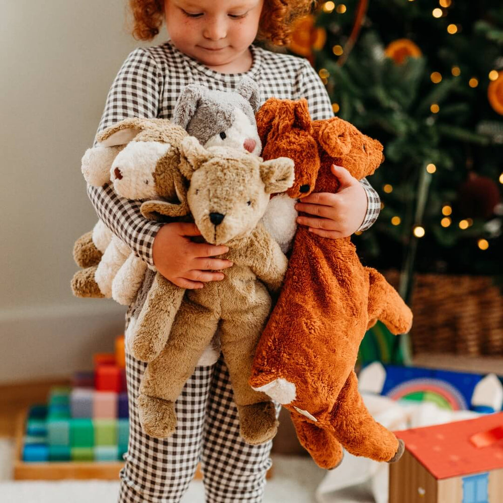 A child holding an armful of Senger organic stuffed animals including the large deer warming pillow.