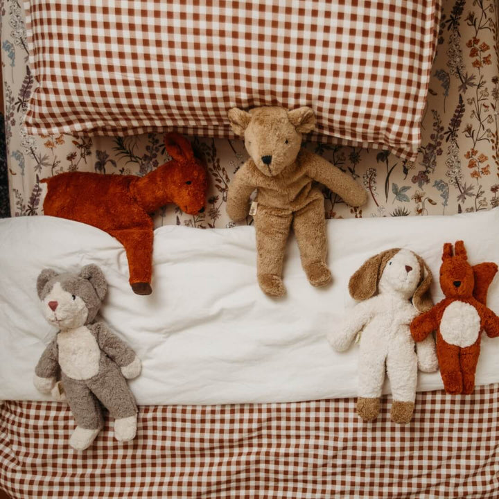 An assortment of Senger organic stuffed animals, including the floppy cat, on a child's bed.