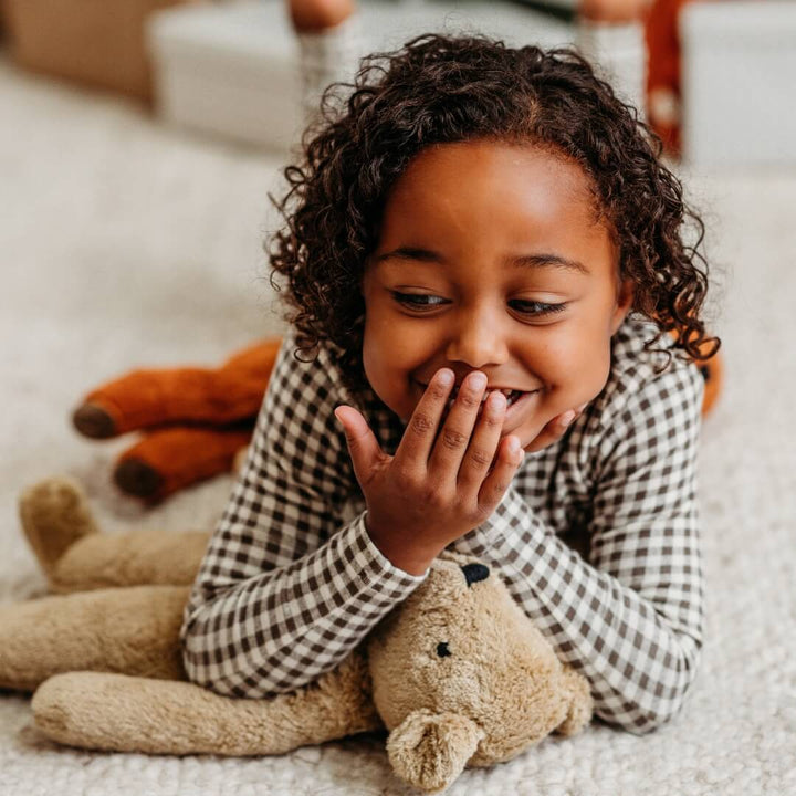 A giggling child snuggled up to an organic teddy bear from Senger.