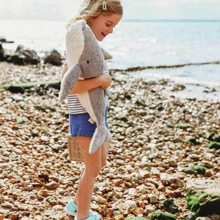 A girl standing on a rocky beach holding a large Senger whale warming pillow