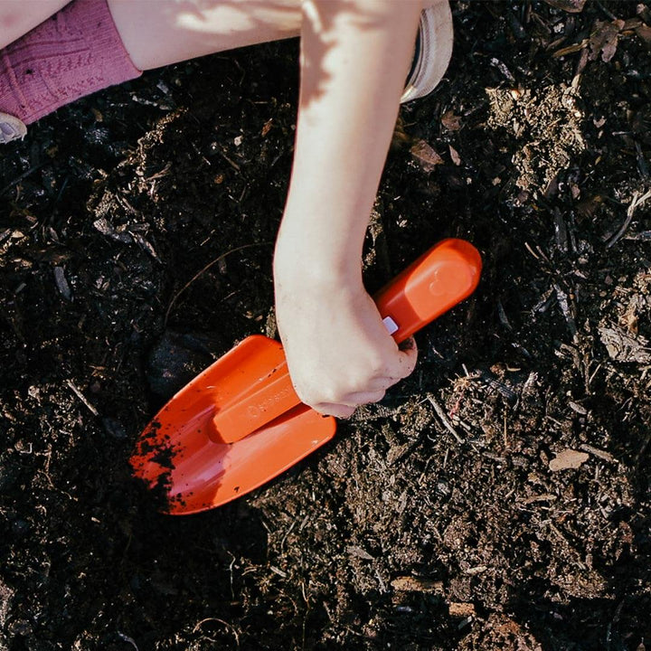 Child digging in mulch with red Spielstabil spade