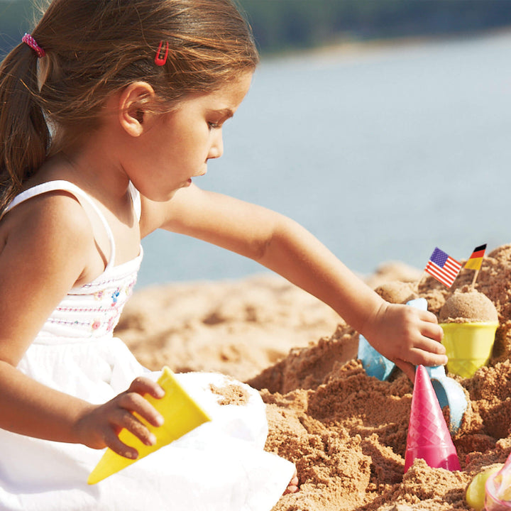 Girl kneeling in the sand scooping sand with a blue scoop into a yellow cone