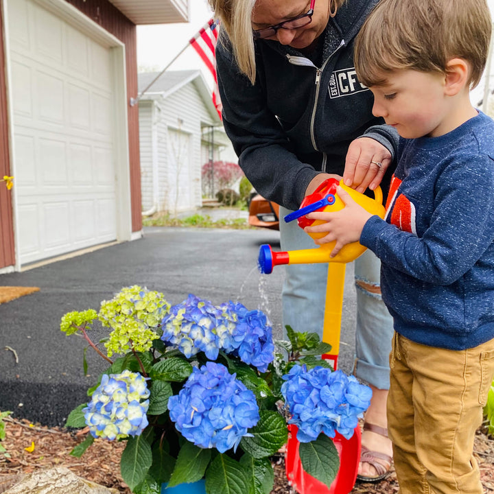 Child pouring water from Spielstabil Watering Can onto blue flowers