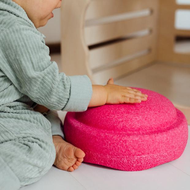 A baby pats the top of a pink Stapelstein stepping stone.