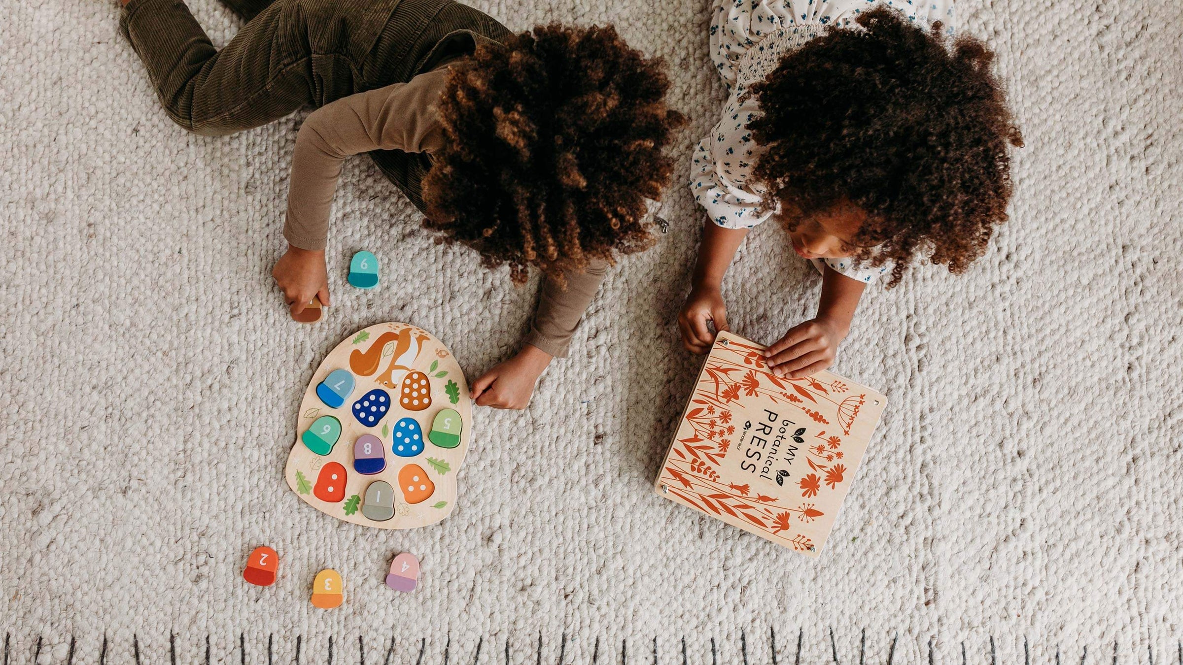 Two children laying on the floor playing with a wooden Tender Leaf Toys Acorn Puzzle and Botanical Press