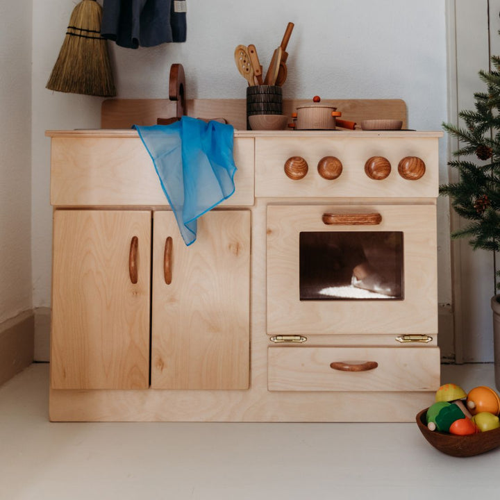 Bella Luna Toys- Wooden Toys and Play Food- Beautiful wooden toy kitchen, with wooden pots and pans on the stove- A bowl with wooden play fruit lies at the bottom right of the stove