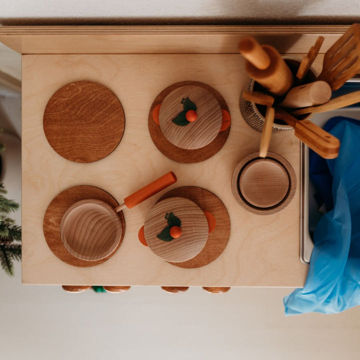 (Top view) Bella Luna Toys- Wooden play stove with wooden burners and wooden pots and pans- To the upper right lies a wooden container containing wooden kitchen tools