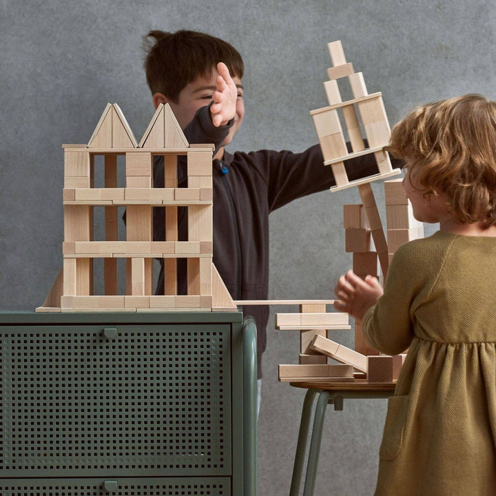 Image of a boy next to a structure made of Clever Up! Unit Wooden Building Blocks 4.0. The child is knocking over another's structure with his hands.